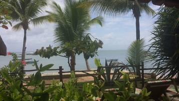 Vista de praia tropical com palmeiras, um deck de madeira e uma cerca de madeira.