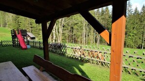 A wooden bench under a shelter with a playground in the background.