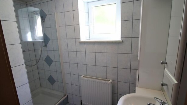 Un baño con ducha, ventana, radiador y lavamanos.