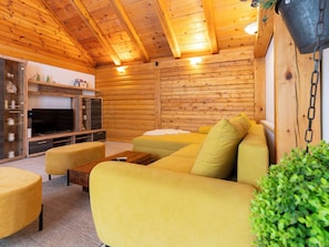 A cozy log cabin interior with a sofa, ottoman, TV, and wooden shelves.