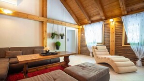 Ein gemütliches Zimmer mit Holzbalkendecke, einem Sofa, einem Liegesessel und einem Tisch mit Pflanzen.