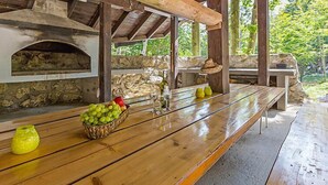 Ein Essbereich im Freien mit einem Steinofen, Holzbänken und einem Tisch mit Obst und Gläsern.