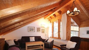 A cozy loft bedroom with a sloped ceiling, wooden beams, a large window, a sofa, a chair, and a small table. - Seekarblick by Interhome (Achenkirch)