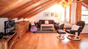 A cozy attic room with wooden beams, a sofa, a chair, a TV, and a window with curtains. - Seekarblick by Interhome (Achenkirch)