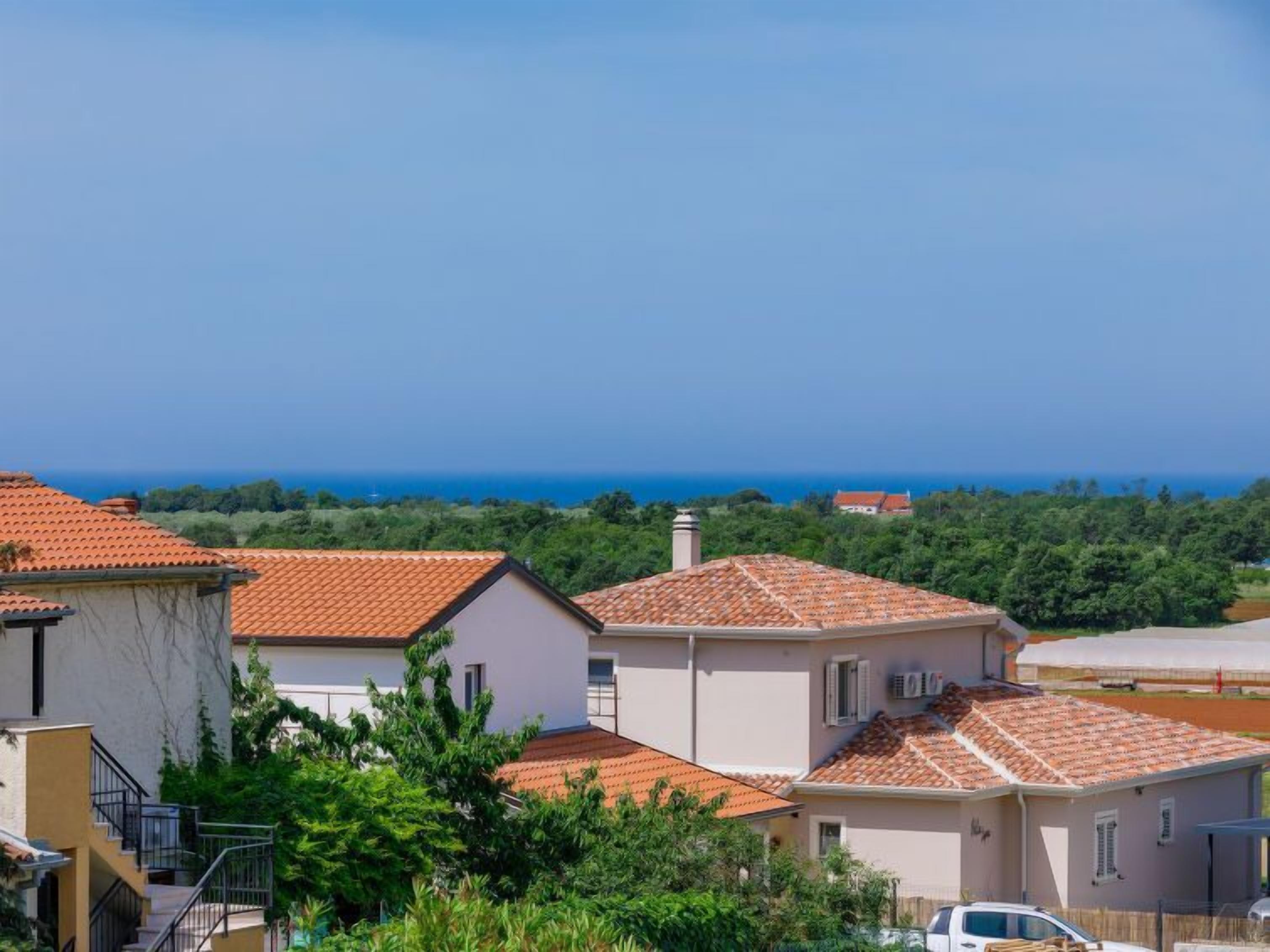 A coastal residential area with terracotta-tiled roofs, white walls, and lush greenery.