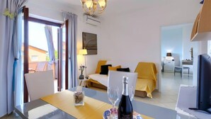 A hotel room with a bed, a dining table with a bottle of wine and glasses, a TV, and a view of the outside. - Apartment Lili by Interhome (Poreč)