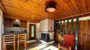 Een gezellig chaletinterieur met een houten plafond, een eethoek met tafel en stoelen, een keuken met houten kastjes en een open haard.