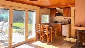 Een houten interieur met een keuken, eethoek en schuiframen naar een tuin.