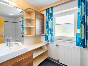 Ett modernt badrum med ett badrumsskåp i trä, en stor spegel och ett fönster med blå gardiner.
