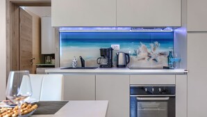 Une cuisine moderne dotée d’une machine à café intégrée, d’une bouilloire et offrant une vue sur l’océan grâce à un pare-éclaboussures en verre.