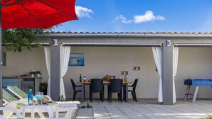 Un espace aménagé au bord de la piscine avec une table et des chaises, un parasol rouge et une table de baby-foot.