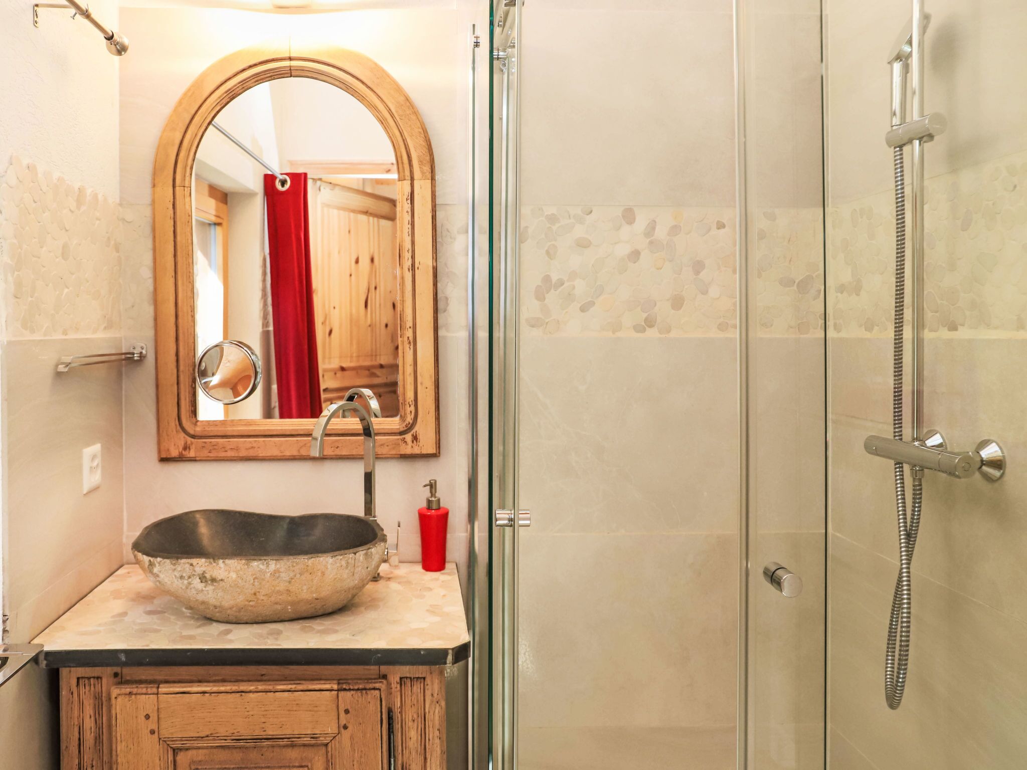 A bathroom with a stone sink, a wooden vanity, a mirror, and a shower enclosure.