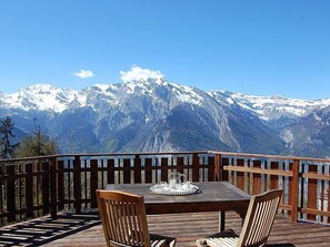 A wooden deck with a table and chairs, overlooking a mountain range with snow-capped peaks. - La Bergerie by Interhome (Nendaz)