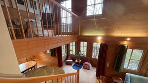 A spacious loft bedroom with a wooden staircase, a large window, and a cozy seating area with a sofa and a small table.