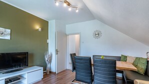 A modern living room with a flat-screen TV, a dining table with chairs, a sofa, and a decorative wall clock.