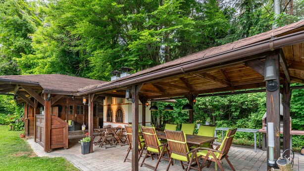 A covered outdoor patio with wooden furniture and a brick floor.