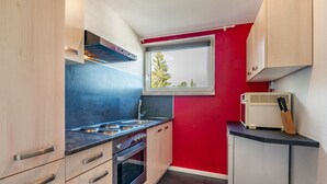 A compact kitchen with a gas stove, oven, and a window with a view of trees.