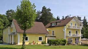 A two-story yellow building with a sloped roof, a balcony on the upper floor, and a well-maintained lawn in front.