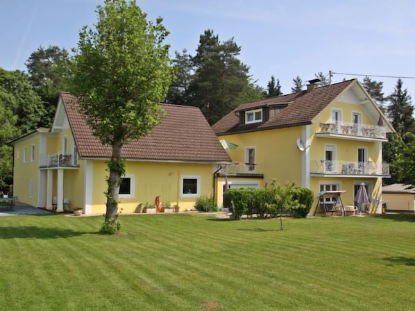 Ein zweistöckiges, gelbes Gebäude mit einem geneigten Dach, einem Balkon im oberen Stockwerk und einem gepflegten Rasen davor.