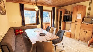 A cozy dining area with a wooden table and chairs, a sofa, and a kitchen area with cabinets and a microwave.