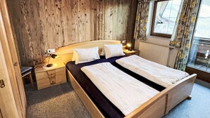 A wooden bed with two pillows, a nightstand with a lamp, and a window with curtains.