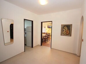Enter a hallway leading to a dining area with a mirror and artwork, featuring a table and chairs, and a TV above.