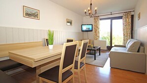 Ein modernes Wohnzimmer mit einem Holzesstisch, zwei Stühlen, einem Sofa, einem Fernseher und einer Kristallleuchtre.