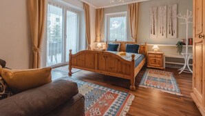 Ein Schlafzimmer mit einem hölzernen Bett, einem Nachttisch, einem Sessel und einem großen Fenster mit Vorhängen.