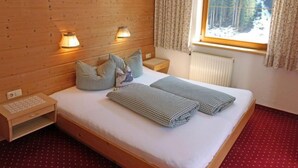 Une pièce chaleureuse aux murs en bois, comprenant un lit, deux lampes de chevet, une table de nuit, un petit bureau et une fenêtre avec des rideaux.