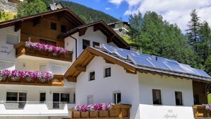 Un bâtiment à deux étages doté de balcons ornés de fleurs, d’une façade en bois et d’un toit recouvert de panneaux solaires.