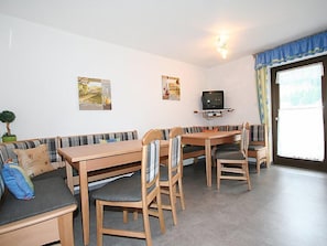 A cozy living room with a sofa, a dining table, and chairs. There is a television on a shelf above the table.