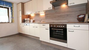 A modern kitchen with white cabinets, a built-in oven, and a window with curtains. - Haslwanter by Interhome (Pians)