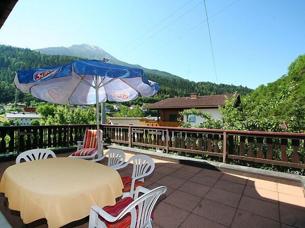 A terrace with a table and chairs, a large umbrella, and a mountain view.