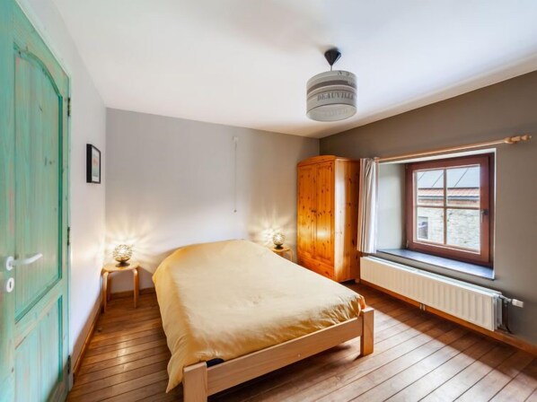 Ein Schlafzimmer mit einem hölzernen Bett, einem Kleiderschrank, einem Heizkörper und einem Fenster mit Blick.