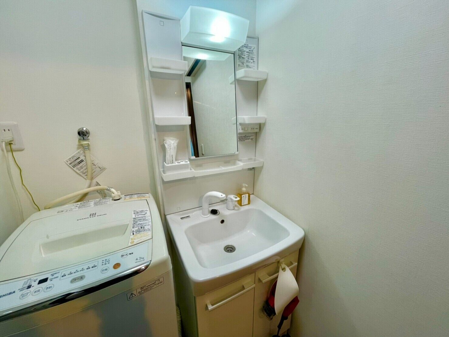 A small bathroom with a washing machine, a sink, and a mirror.
