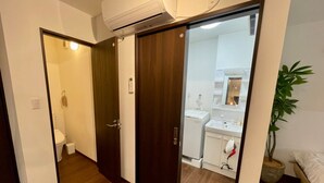 Een kamer met een houten vloer, een wit toilet, een witte wastafel en een bed.
