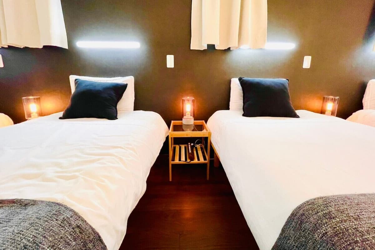 A hotel room with two single beds, each with a pillow and a bedside table with a lamp.