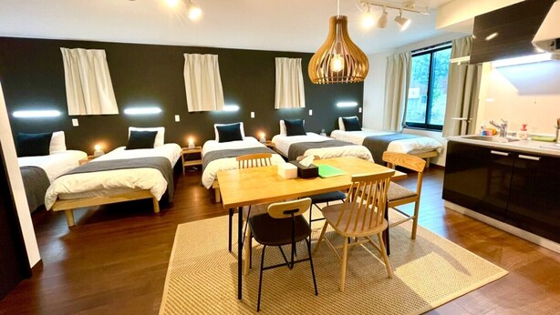 Een moderne hotelkamer met vier eenpersoonsbedden, een houten eettafel en een kitchenette.