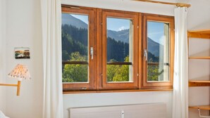 Ein Schlafzimmer mit Bett, einem Fenster mit Bergblick, einem Nachttisch und einer Lampe.