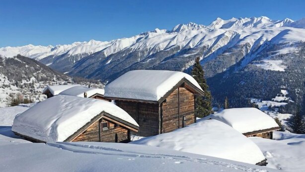 Eine Holzhütte mit schneebedecktem Dach, umgeben von schneebedeckten Bergen und Bäumen.