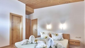 Un dormitorio con techo de madera, una cama con almohadas florales, dos puertas de madera y luces fijadas a la pared.