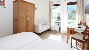 A bedroom with a bed, a wooden wardrobe, a white sofa, a dining table with chairs, and a window with a view of the outside. - Apartment Liebl by Interhome (Seefeld in Tirol)