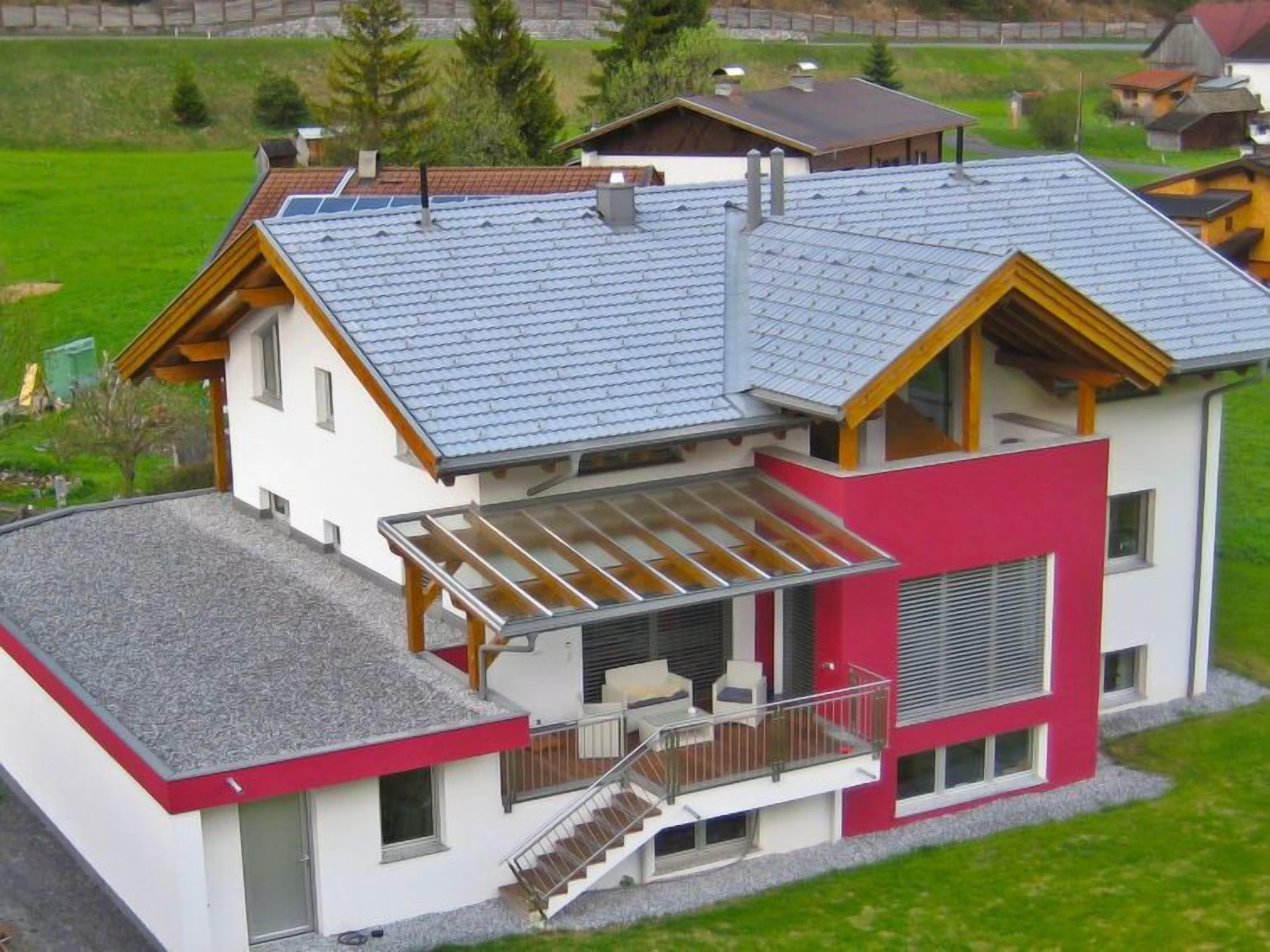 A modern two-story house with a sloped roof, a balcony, and a covered outdoor seating area.