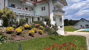 A two-story building with a balcony, surrounded by a well-maintained garden with various flowers and shrubs.