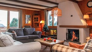 A cozy living room with a fireplace, wooden beams, and a large window. - Les Etoiles by Interhome (Nendaz)