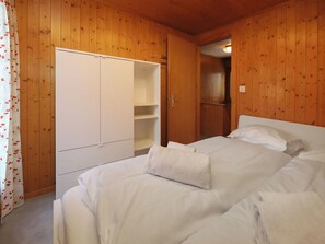 Ein Schlafzimmer mit Bett, weißen Vorhängen, einem Kleiderschrank und einer Holzbalkendecke.