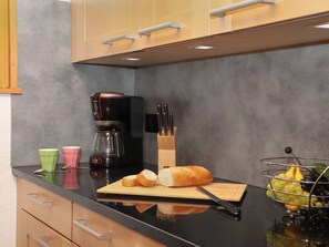 Cozinha com cafeteira, tábua de corte com pão e faca, fruteira e porta-facas.