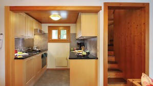 A compact kitchen with wooden cabinets, a central island, and a window above the sink. - Coucordin by Interhome (Nendaz)
