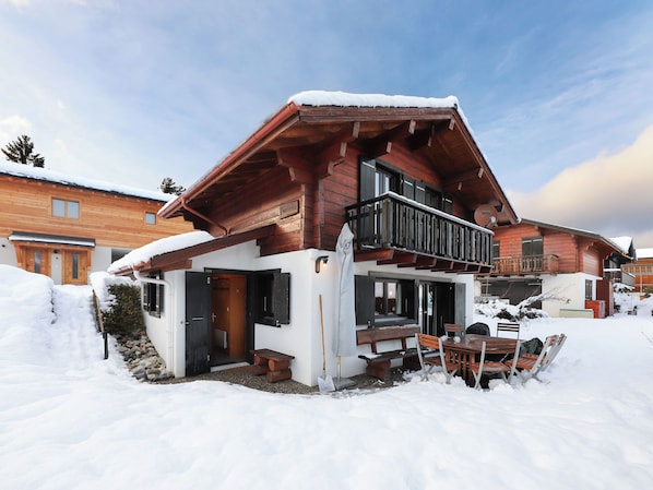 Eine Holzhütte mit Balkon und einer Holzterrasse, vor einer verschneiten Landschaft.