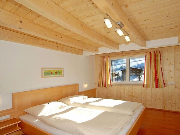 A wooden-paneled bedroom with a bed, a window with curtains, and a framed picture on the wall.